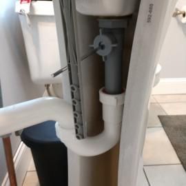 Exposed white and grey plastic drain plumbing under a pedestal bathroom sink, next to a white toilet.