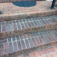 Two steps made of dark, rustic bricks leading to a landing with a semicircular black welcome mat.