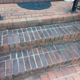 A front view of two brick stairs leading to a landing with a dark, oval patterned doormat.