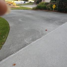 A concrete driveway split into two sections, with one side freshly cleaned and the other side darker and weathered.