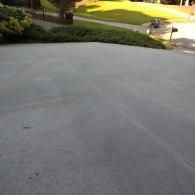 An elevated view of a gray concrete driveway leading to a lush green lawn on a sunny day.