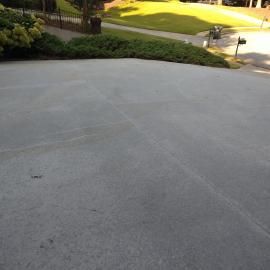 An expanse of grey concrete driveway leading to a grassy lawn and residential street in the background.