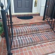 A set of outdoor red brick stairs leading to a dark gray front door, flanked by black metal railings.