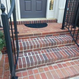 Three steps made of multi-toned red bricks lead up to a doorway with a dark mat.