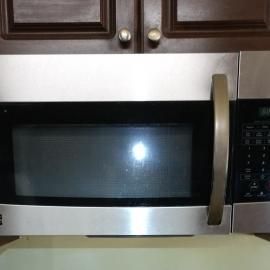 A stainless steel over-the-range microwave installed below dark wooden cabinets.