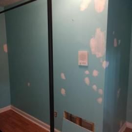 Turquoise interior wall with drywall patching, a rectangular vent opening, and a hanging white instructional sign.
