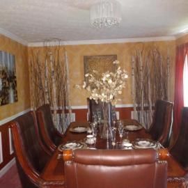 A formal dining room features a dark wood table with brown leather chairs, decorative birch branches, and a floral centerpiece.