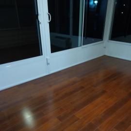 Polished wooden floorboards in a room featuring large glass sliding doors with white frames leading to an outdoor space.
