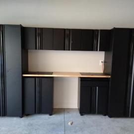 Black garage cabinetry with a light wood countertop, featuring two tall cabinets, upper wall units, and base cabinets.