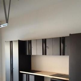 Dark metallic garage cabinets with a workspace counter and overhead storage mounted on a plain white wall.