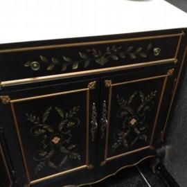 Black wooden cabinet with gold-painted floral detailing, ornate metal handles, and a white countertop.