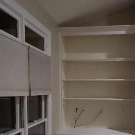 Off-white built-in shelves next to a window covered by light-colored pleated shades.