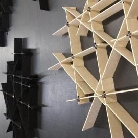 Two modular, geometric shelving units, one light wood and one black, mounted on a dark grey wall.