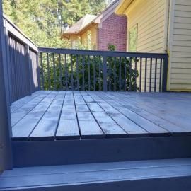 A dark-stained wooden deck with railings leading to stairs, situated next to yellow and purple house siding.
