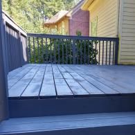 A wooden deck with blue-painted stairs and railings, leading to a yellow-sided house with a visible roofline.