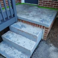 Concrete porch steps with weathered grey paint showing heavy wear, attached to a brick house exterior.