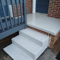 Freshly painted light-gray concrete steps and a landing leading to a home entrance with a blue porch railing.