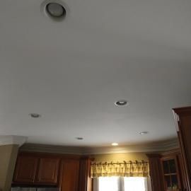 A kitchen ceiling with recessed lights, wooden cabinets, and a window with a valance below.