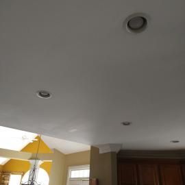 A white ceiling with four recessed lights and a partial view of a room with yellow walls and a dark wooden cabinet.