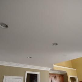 A white ceiling featuring three recessed circular lights, with tan walls and white trim visible underneath.