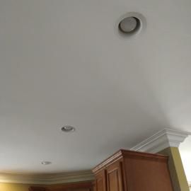 White ceiling with recessed lighting above wooden kitchen cabinets and decorative crown molding.