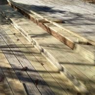 A wooden deck with a raised platform or bench under construction, featuring light-colored planks and long shadows.