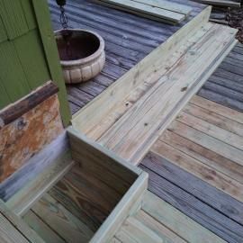 New light-colored wooden deck boards installed next to older, weathered gray boards beside a green wall and planter.