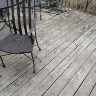 A metal patio chair sits on a weathered wooden deck with diagonal planks.