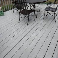 A metal patio table and four matching chairs sit on a light gray painted wooden deck.