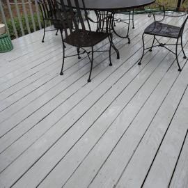 A gray painted wooden deck with a black metal patio table and matching chairs under a railing.