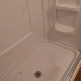 A clean white shower stall with a built-in shelf and a drain in the floor.