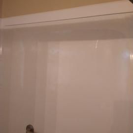 A plain, white shower enclosure wall with a smooth, glossy finish and a horizontal top trim.