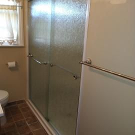 A bathroom featuring a glass-door shower, a partial view of a toilet, brown tile flooring, and a towel bar on the wall.
