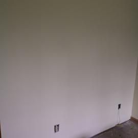 A white wall with two electrical outlets, one near the floor and one higher up, in an unfinished room.