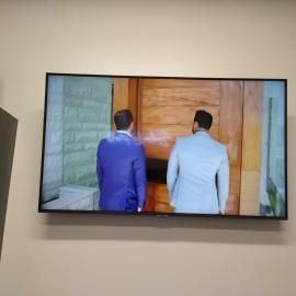 Two men in light-colored suits stand with their backs to the camera, facing a large wooden door inside a building.