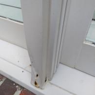 Close-up of a white painted wooden window frame showing signs of rot, peeling paint, and water damage at the bottom base.