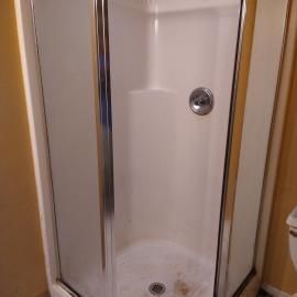 A corner shower stall with white walls, a circular silver handle, and glass doors against yellow walls.
