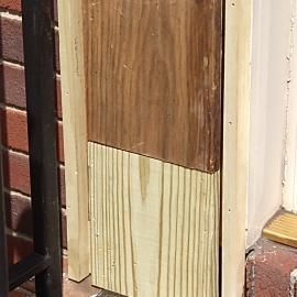A repair on a wooden post showing a section of new, light-colored wood joined to an existing dark, weathered wood section.