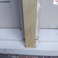 A vertical wooden post rests on a light-colored surface with caulk applied at the base.