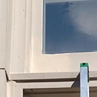 Close-up of a white window frame with a metal ladder leaning against the exterior trim.