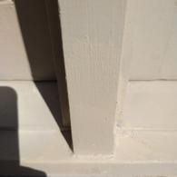 A white painted wooden post meeting a horizontal base, casting a dark, sharp-edged shadow to its left.