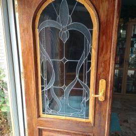 A wooden door featuring an arched, stained glass panel with flowing, etched line patterns and a gold-tone lever handle.