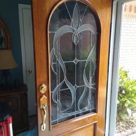 A wooden front door with an arched glass panel featuring a decorative, etched swirling design, with brass hardware.