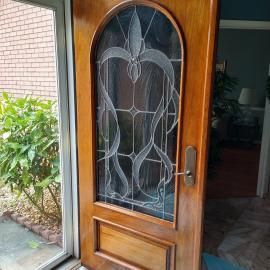 A wooden front door with an arched glass panel featuring an intricate, swirling etched design, viewed from the inside.