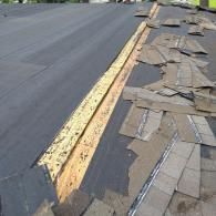 A roof under renovation, showing exposed plywood decking along the ridge with new underlayment next to old shingles.