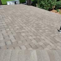 A ground-level view of a light brown, rectangular-paver patio extending toward a grassy yard and a small white pool.