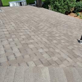 A view looking down a pitched residential roof covered in light brown and gray asphalt shingles.