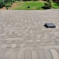 A paved stone patio with a gray, rectangular drainage cover, leading to a grassy yard with landscaping.