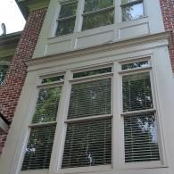 A low-angle view of two stories of white-trimmed windows on a brick exterior wall, featuring closed wooden blinds.