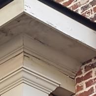 Close-up of a weathered, beige wooden corner molding on a building exterior with peeling paint and cracks at the joints.